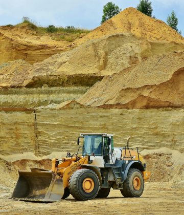 An excavator working in an open pit mine surrounded by sandy terrain and clear sky.